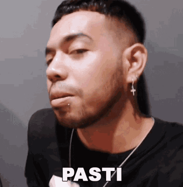 a man with a beard and cross earrings is making a funny face and says pasti .
