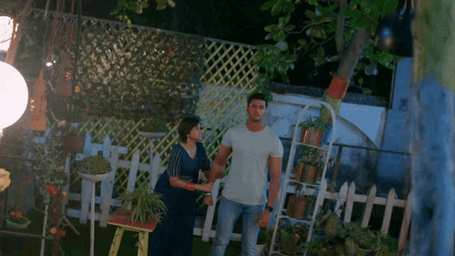 a man and a woman standing in a garden with potted plants