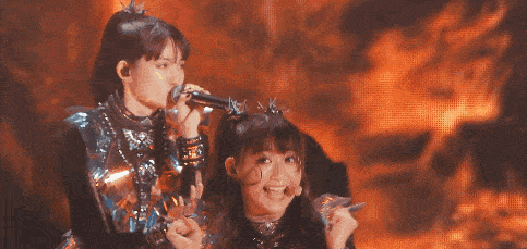 two girls are singing into microphones in front of a flaming background