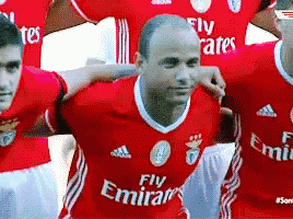 a man wearing a fly emirates jersey stands with his arms around another man