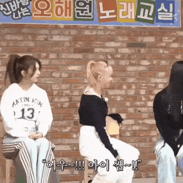 a group of girls are sitting in front of a brick wall and talking to each other .