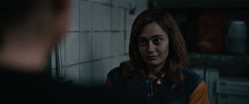 a woman in a blue and orange jacket looks at a man