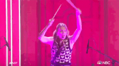 a woman is playing drums on a stage in front of a pink background .