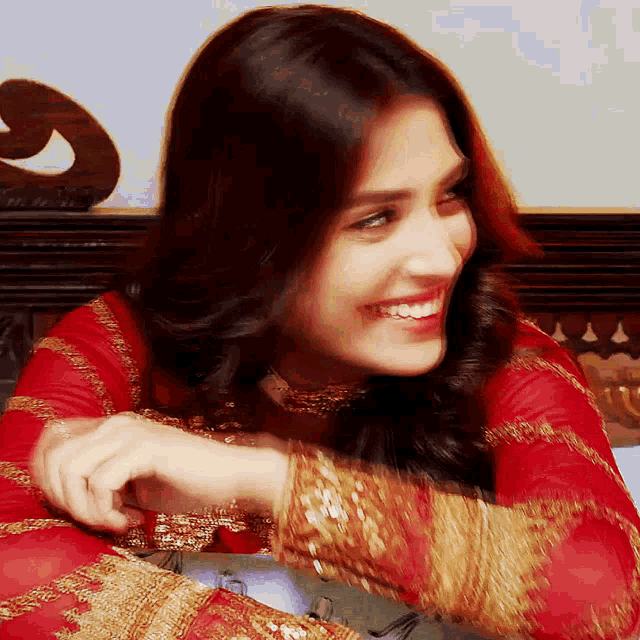 a woman in a red and gold dress is smiling and looking down