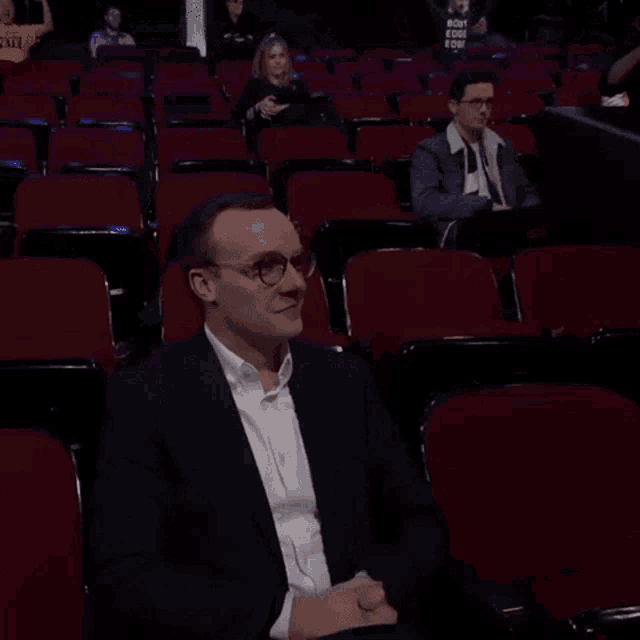 a man in a suit gives a thumbs up in a theater