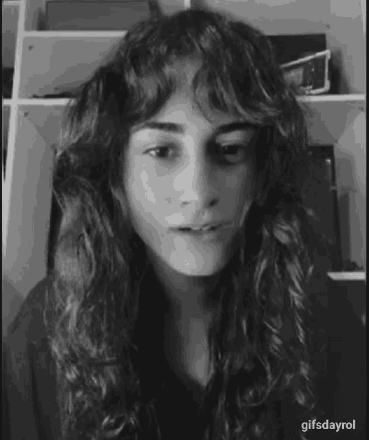 a black and white photo of a woman with long curly hair making a face .