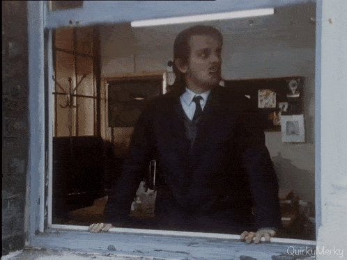 a man in a suit and tie is looking out of a window with quirky merky written below him