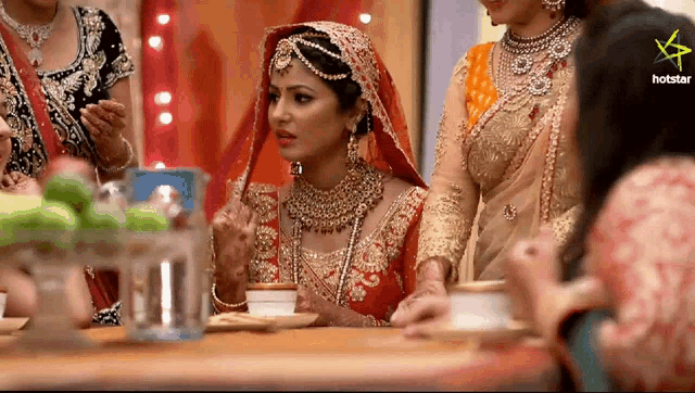a bride in a red and gold dress sits at a table with other women
