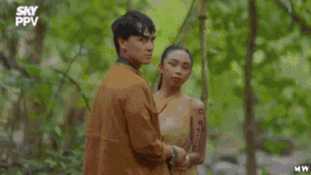 a man and a woman are standing in a forest holding hands .