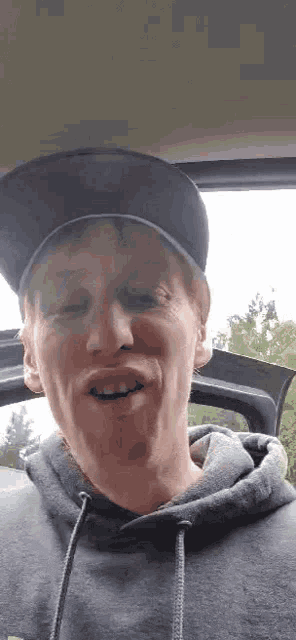 a man wearing a hat and a hoodie is making a funny face while sitting in the back of a car .