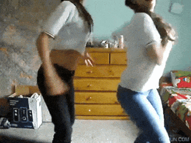 two women are dancing in a bedroom with a box of speakers in the background and the website giffun.com visible