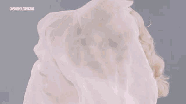 a drag queen with blonde hair and red lips is wearing a white dress and holding a white cloth in her hand .