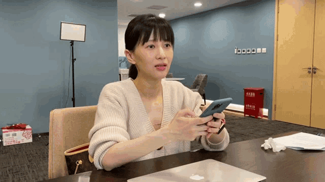 a woman sits at a table holding a cell phone