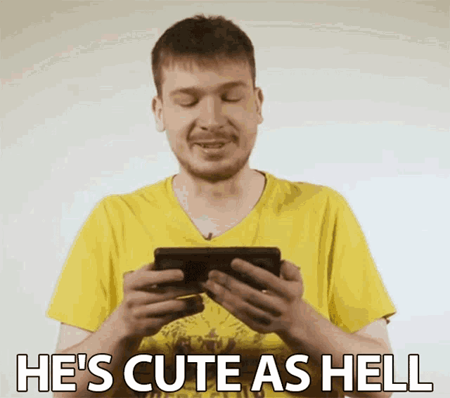 a man in a yellow shirt is holding a cell phone with the words he 's cute as hell above him