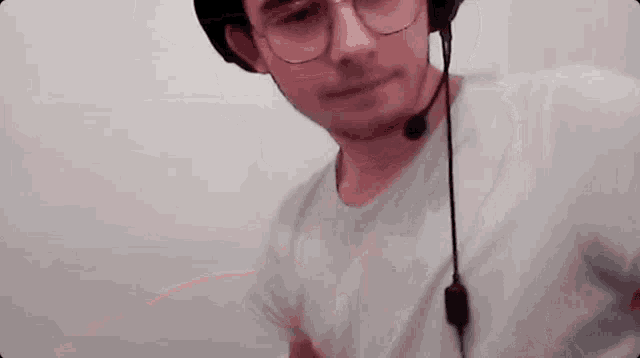 a man wearing glasses and a hat with a microphone on his head is standing in front of a white wall .