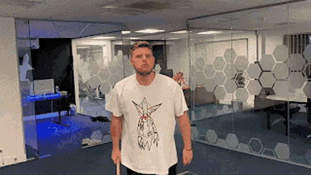 a man in a white shirt with a bird on it is standing in an office