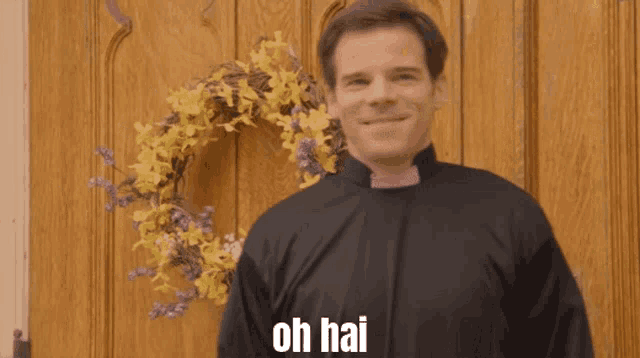 a priest standing in front of a door with a wreath on it and the words oh hai on his shirt