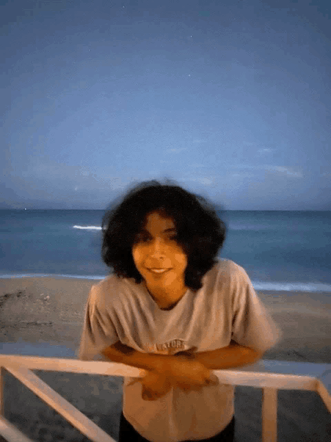 a young man wearing a t-shirt that says ' surfer ' on it stands on a balcony overlooking the ocean