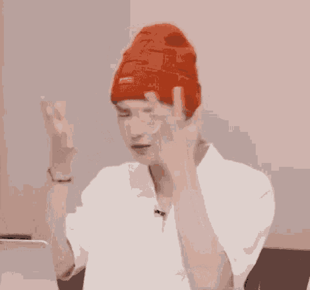 a man wearing a red hat and a white shirt is holding his hands to his head .