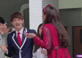 a group of people are standing next to each other and a woman in a red dress is giving a man a flower .