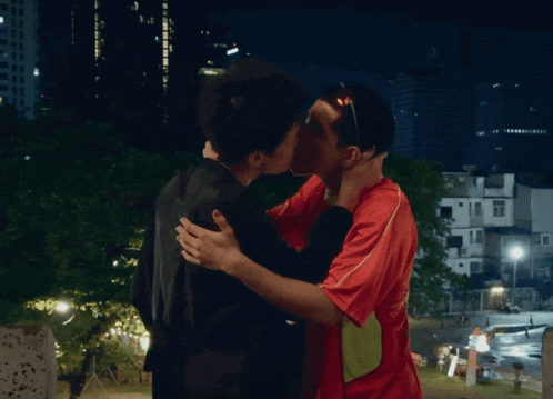 a man in a red shirt is kissing another man in a black shirt