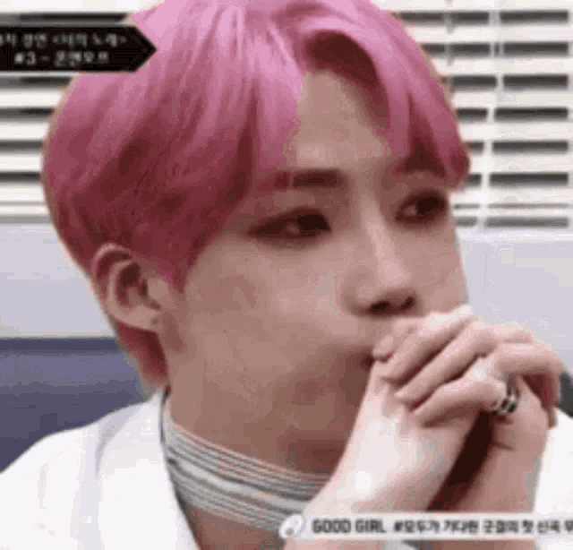 a young man with pink hair is covering his mouth with his hands while wearing a choker .
