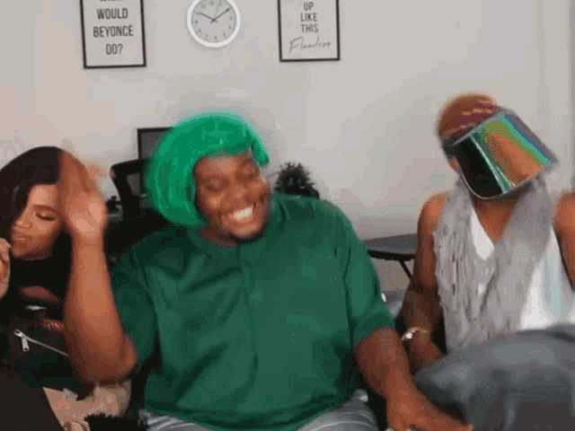 a man wearing a green wig is sitting in a room with two other people .