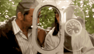 a man and a woman are kissing in front of a mirror with a clock on it .