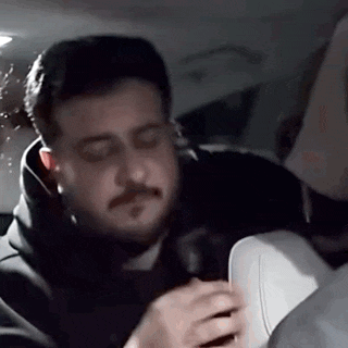 a man with a beard is sitting in the back seat of a car with his eyes closed .