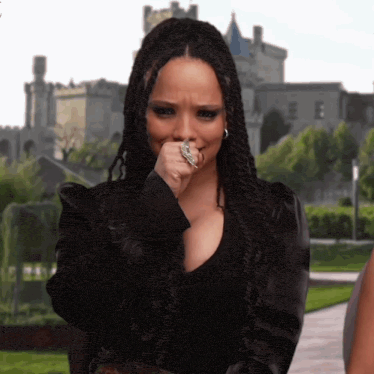 a woman with braids and a ring on her finger is covering her mouth with her hand .