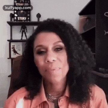 a woman with curly hair is sitting in a chair in front of a bookshelf .
