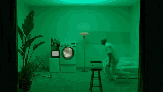 a man is dancing in a green room in front of a washing machine .