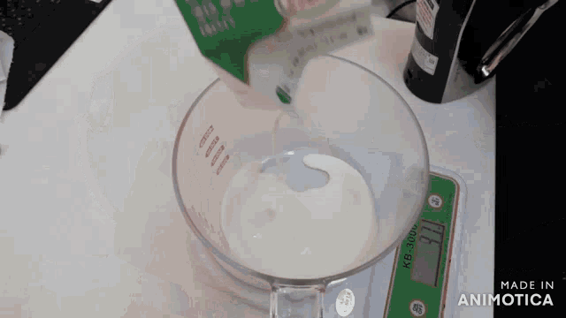 a measuring cup filled with milk is being poured into a digital scale that says kg-3100 on it