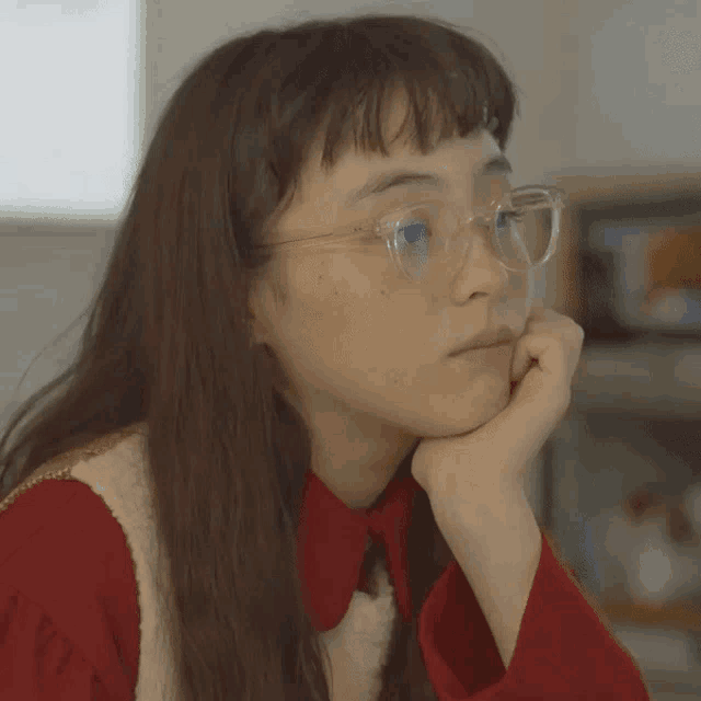a woman wearing glasses and a red shirt is resting her head on her hand