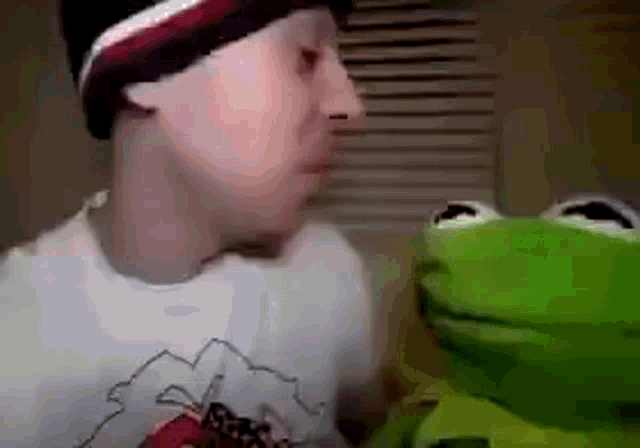 a man and a kermit the frog are looking at each other and kissing .