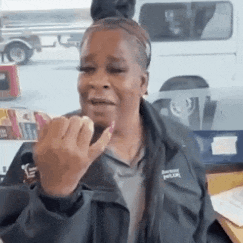 a woman in a black jacket is making a funny face while sitting at a desk .
