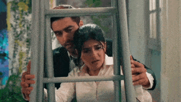a man and a woman are standing next to each other in a room behind a ladder .
