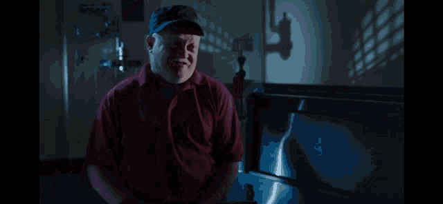 a man in a red shirt and black hat is sitting in front of a sink
