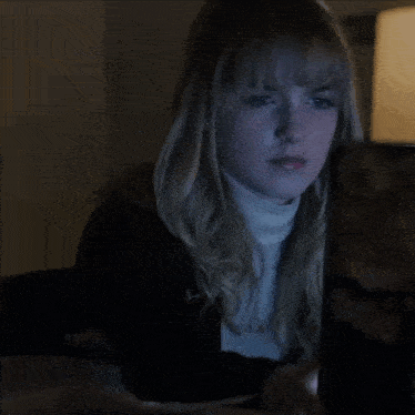 a woman in a black jacket and white turtleneck is looking down at something