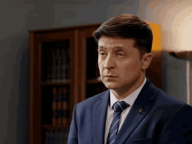 a man in a suit and tie is standing in front of a book shelf .