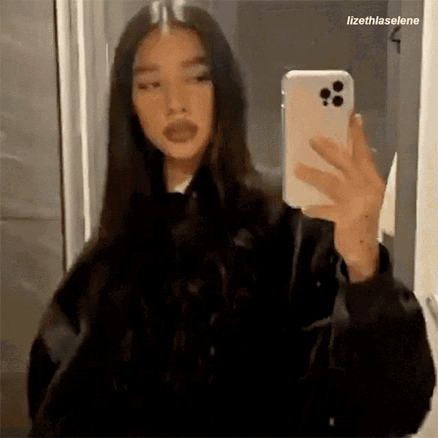 a woman is taking a selfie with her cell phone in a mirror .