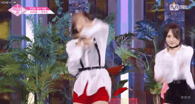 a woman in a white shirt and red shorts is dancing on a stage with palm trees in the background .