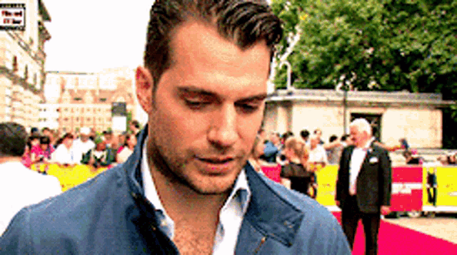a man in a blue jacket is standing on a red carpet in front of a crowd .