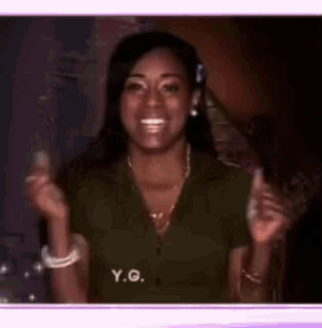 a woman in a green shirt with the word y.g. on it is smiling and giving a thumbs up .