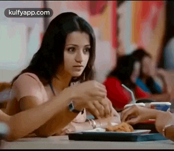 a woman is sitting at a table in a restaurant eating a chicken sandwich .