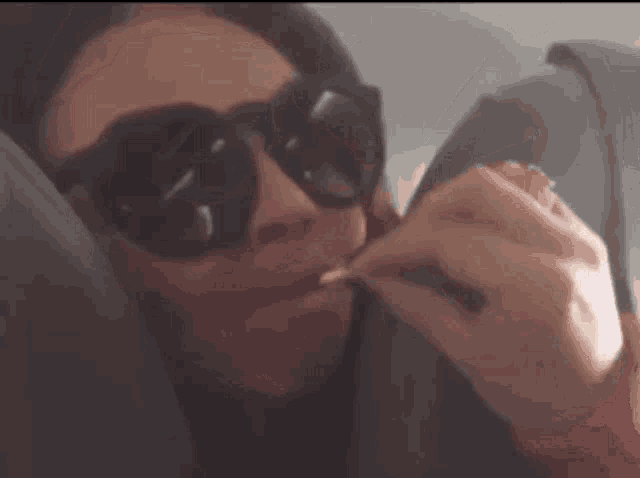a woman wearing sunglasses and a ring is holding something in her mouth