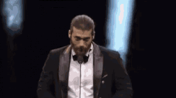 a man in a tuxedo is speaking into a microphone .