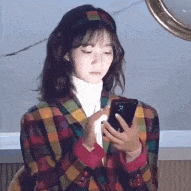 a woman in a plaid jacket is using a cell phone .