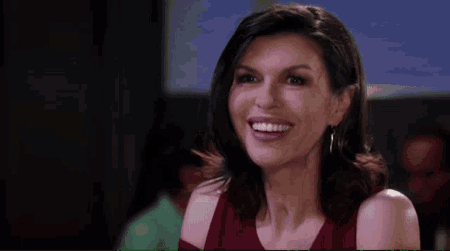 a woman wearing a red top and earrings smiles at the camera