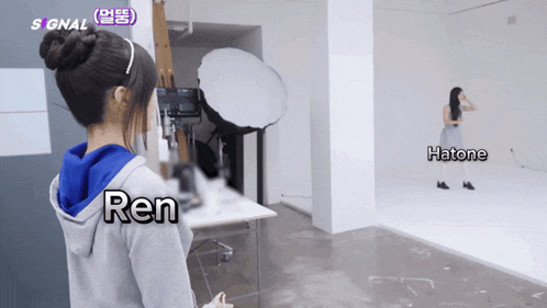 a woman in a gray hoodie stands in front of a camera with the name ren written on her back
